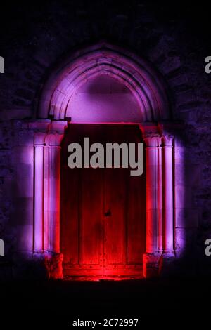 Sessione di pittura leggera in un luogo mistico la notte. Porta in legno di una chiesa con scultura gotica illuminata con led. Foto Stock