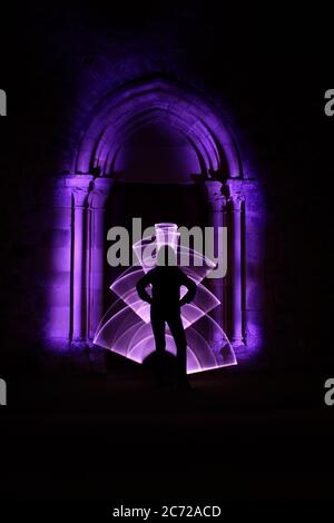 Silhouette di una donna davanti ad un arco scolpito in pietra. Forma astratta ricurva realizzata con violetto chiaro. Sessione di pittura leggera di notte. Foto Stock