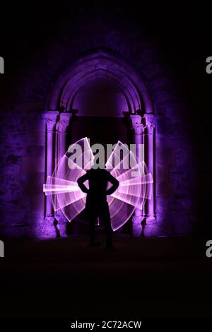 Silhouette di una donna davanti ad un arco scolpito in pietra. Forma astratta ricurva realizzata con violetto chiaro. Sessione di pittura leggera di notte. Foto Stock