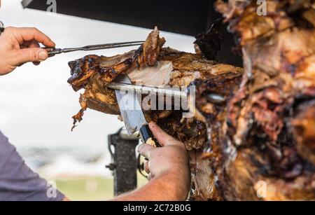 Porzionamento di maiale arrosto, affettamento di carne.. Maiale grigliato carbone tradizionale e fuoco. Il maiale viene arrostito intero su un fuoco aperto. Maiale sullo spiedo. Foto Stock