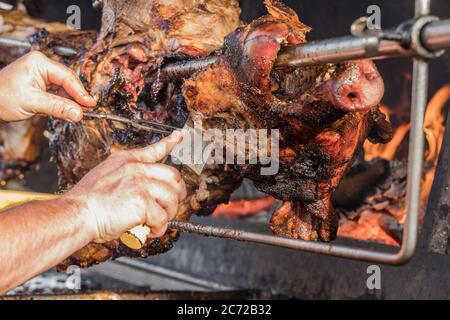 Porzionamento di maiale arrosto, affettamento di carne.. Maiale grigliato carbone tradizionale e fuoco. Il maiale viene arrostito intero su un fuoco aperto. Maiale sullo spiedo. Foto Stock