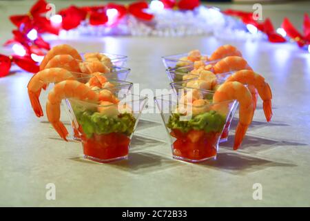 Aperitivo bicchieri di gamberi su avocado e pomodoro con due verrines di taramasalata e salmone pesce con sfondo decorazioni illuminato Foto Stock