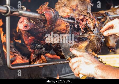 Porzionamento di maiale arrosto, affettamento di carne.. Maiale grigliato carbone tradizionale e fuoco. Il maiale viene arrostito intero su un fuoco aperto. Maiale sullo spiedo. Foto Stock