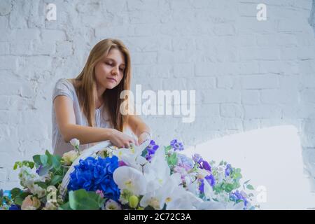 Ritratto di artista floreale donna professionista, fiorista che fa grande cesto floreale con fiori in officina, negozio di fiori. Floristry, fatto a mano, matrimonio Foto Stock