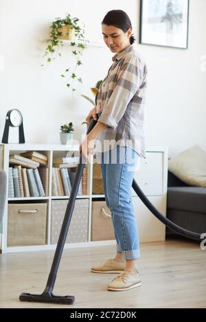Giovane donna che usa l'aspirapolvere per i lavori domestici aspira il pavimento a casa Foto Stock