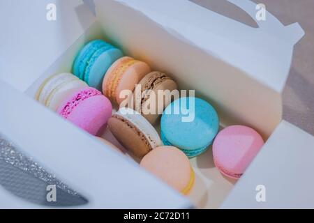 Macaroon colorati in scatola regalo bianca sul tavolo presso il negozio di caramelle, il mercato, il caffè o la panetteria - vista ravvicinata. Dessert, biscotti, dolci e tradizionali Foto Stock