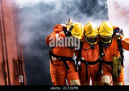 I vigili del fuoco asiatici salvano il loro collega di squadra da costruzione bruciante. Misure di sicurezza per vigili del fuoco contro incidenti e concetto di servizio pubblico. Foto Stock
