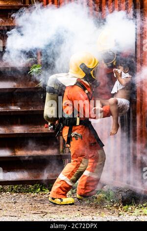 Pompiere salvataggio ragazza bambino piccolo da costruzione in fiamme. Tiene la ragazza e la salva attraverso la finestra di costruzione. Soccorso di sicurezza dei vigili del fuoco da Foto Stock