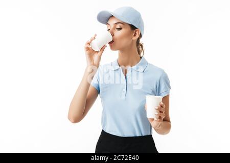 Giovane bella donna in polo blu T-shirt e cappuccio bere da tazza monouso su sfondo bianco Foto Stock