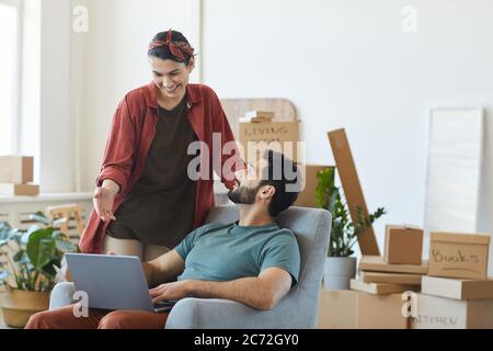 Giovane coppia felice che usa il computer portatile insieme mentre si trasferiscono al nuovo appartamento Foto Stock