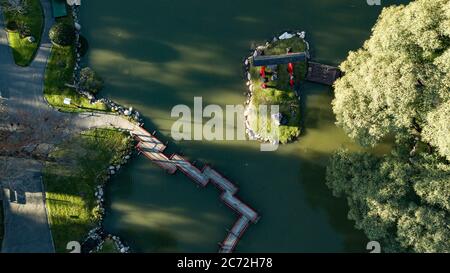 Una vista aerea dall'alto sul ponte rosso e termoretraibile in stile giapponese sulle acque verdi del lago durante il tramonto in una giornata di sole. Foto Stock