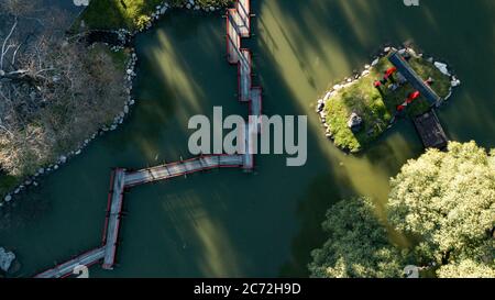 Una vista aerea dall'alto sul ponte rosso e termoretraibile in stile giapponese sulle acque verdi del lago durante il tramonto in una giornata di sole. Foto Stock