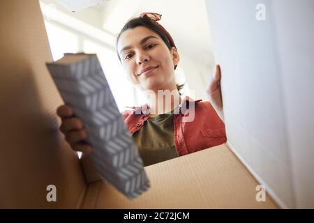 Giovane donna bella che disimballa i libri dalla scatola durante il suo trasferimento a nuova casa Foto Stock