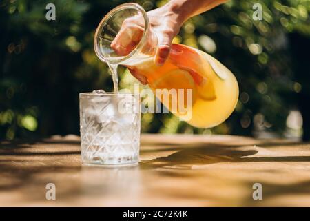 Bicchiere di limonata con ghiaccio su tavolino nel cortile estivo. Foto Stock