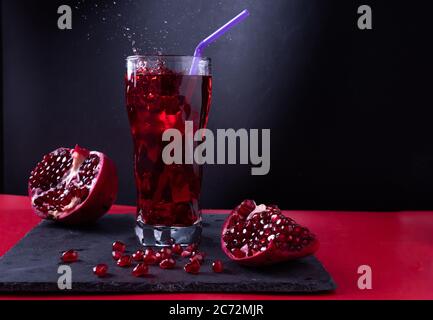 Succo di melograno su sfondo nero e tavolo rosso. Succo di melograno luminoso in un bicchiere. Foto Stock