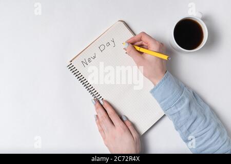 Donna scrive in taccuino l'iscrizione NUOVO GIORNO. Testo scritto a mano. Vista dall'alto del blocco note e della tazza di caffè. Foto Stock