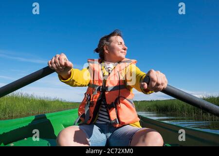 Donna che paddling una barca attraverso il fiume in giornata di sole Foto Stock