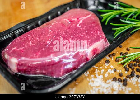 Bistecca di manzo in confezionamento sottovuoto e spezie su tagliere di legno Foto Stock