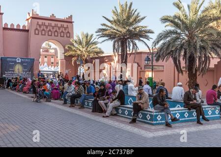 Persone che siedono fuori del luogo al-Mouahidine nel centro di Ouarzazate, Marocco, in attesa dell'apertura del 4 ° Rencontre Nationale d'Artisanat. Foto Stock