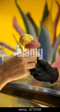 Venditore in grembiule che tiene il gelato in un cono del waffle, primo piano. Vendita di gelato in un negozio Foto Stock
