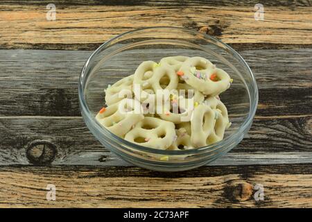 Pretzel immersi in cioccolato bianco con spruzzini in recipiente di vetro sul tavolo Foto Stock