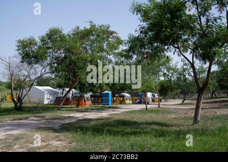 Matamoros, Messico. 13 luglio 2020. La zona di isolamento è vista da lontano. La zona di isolamento dista 100 metri dal campo principale per rifugiati. Attualmente ci sono 23 persone che aspettano in isolamento per essere testate o per i risultati dei loro test del coronavirus. 3 dei residenti del campo hanno provato positivi per il virus. Ci sono circa 1,500 persone che vivono in tende all'interno di una zona recintata fuori del parco mentre attendono le loro audizioni di asilo negli Stati Uniti d'America. Credit: Cripps/Alamy Live News Foto Stock