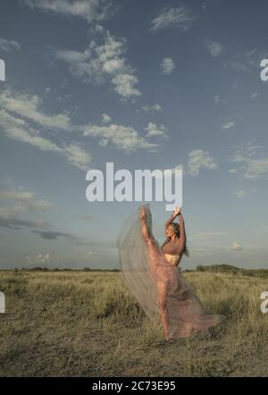 Una moderna ballerina che si esibisce in natura. Ballerina o ballerina moderna in un abito di seta rosa danzante in natura. Foto Stock