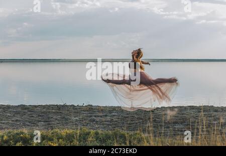 Una moderna ballerina che si esibisce in natura. Ballerina o ballerina moderna in un abito di seta rosa danzante in natura. Foto Stock