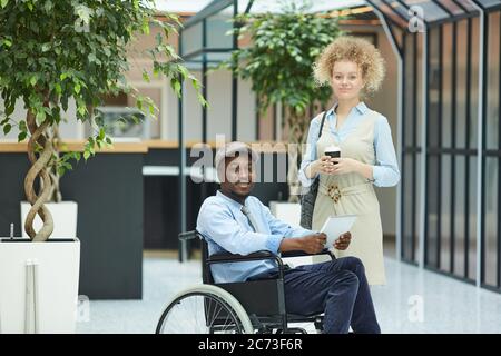 Ritratto di coppia multietnica guardando la macchina fotografica mentre si trova nel centro commerciale giovane donna in piedi vicino a disabili africano uomo Foto Stock