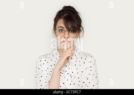 Bella donna brunetta con occhiali che gesturano il segno del silenzio su una parete bianca studio guardando la macchina fotografica Foto Stock