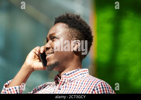 Uomo sorridente africano che parla sul telefono cellulare mentre cammina all'aperto Foto Stock