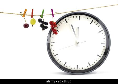 Orologio che mostra cinque minuti a dodici con una ciliegia fresca, uva spina, rosso e nero ribes appeso su una linea di vestiti picchetti in una dieta sana con Foto Stock