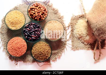 Riso fuori da piccolo sacco isolato su sfondo bianco. Diverso impulso colorato in ciotole. Cazzo pisello, rene rosso, lenticchie, semi di Fenugreek, grano Dalia, Foto Stock