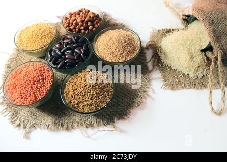 Riso fuori da piccolo sacco isolato su sfondo bianco. Diverso impulso colorato in ciotole. Cazzo pisello, rene rosso, lenticchie, semi di Fenugreek, grano Dalia, Foto Stock