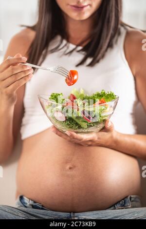 La ragazza incinta mangia l'insalata da una ciotola in mano. Foto Stock