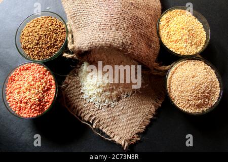 Riso fuori da piccolo sacco isolato su sfondo nero. Un tocco di colore diverso in una ciotola. Lenticchie, semi di Fenugreek, dalia di grano, pisello piccione Foto Stock