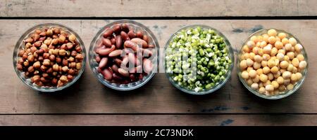 Raccolta di legumi (ceci, piselli verdi, fagioli verdi, rene rosso, piselli secchi) in diverse ciotole isolate su sfondo di legno. Foto Stock