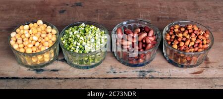 Raccolta di legumi (ceci, piselli verdi, fagioli verdi, rene rosso, piselli secchi) in diverse ciotole isolate su sfondo di legno. Foto Stock