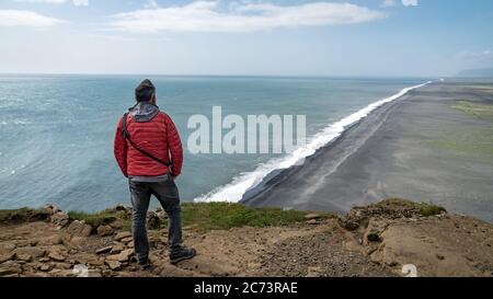 Uomo non identificato che si affaccia sulla spiaggia di sabbia nera vulcanica infinita situato in Vik Islanda Foto Stock