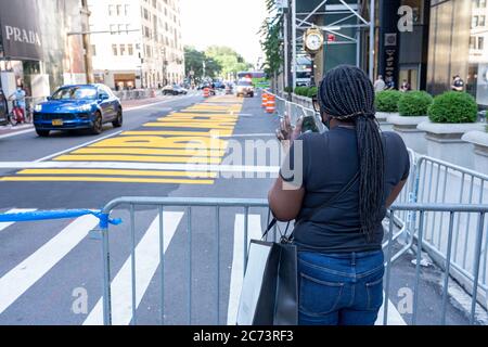 Un passerby scatta foto di un murale Black Lives Matter dipinto sulla Quinta Avenue di fronte alla Trump Tower di New York. Come uno di una serie di murales Black Lives Matter da dipingere in tutti e cinque i quartieri di New York City attira turisti e manifestanti su entrambi i lati del movimento politico. Foto Stock