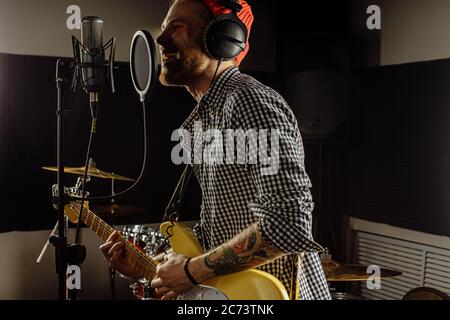 giovane musicista professionista caucasico che suona la chitarra e canta sul microfono. bel ragazzo appassionato di musica, si sta preparando per il concerto rock in recordin Foto Stock