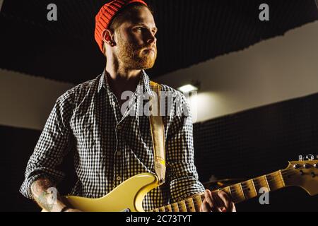 il musicista caucasico di talento suona sulla chitarra elettrica la sua canzone preferita, l'esecutore di musica rock che pratica prima di un concerto in studio di registrazione Foto Stock