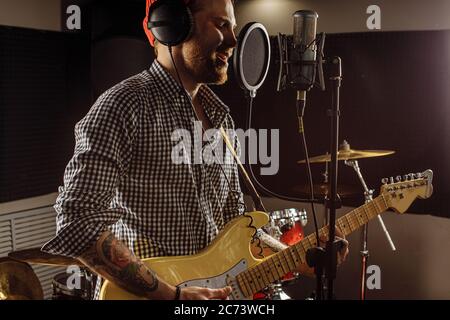 un musicista caucasico impressionante suona la chitarra elettrica e canta in studio di registrazione. uomo che prepara, praticando prima della performance musicale, prima del concerto. musi Foto Stock