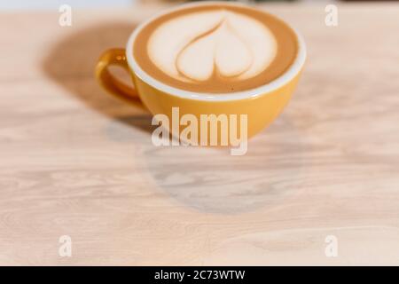 Magnifica tazza gialla di piccole dimensioni di cappuccino fresco aromatico o latte si erge su un banco di legno di colore chiaro nella moderna caffetteria, con caffè art Foto Stock