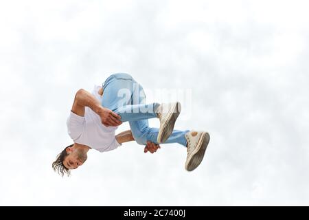 Fitness Guy fare trucco parkour mentre saltando in aria, foto a lunghezza intera Foto Stock