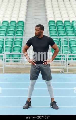 attraente giovane sportivo africano in shorts. t-shirt che tiene le braccia sui fianchi, guardando da parte, full length photo.leisure concetto Foto Stock