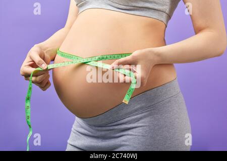 Donna incinta che misura la sua grande pancia sul terzo trimestre con nastro, ripresa tagliata. Pancia di donna incinta primo piano. Immagine di cura prenatale, maternità Foto Stock