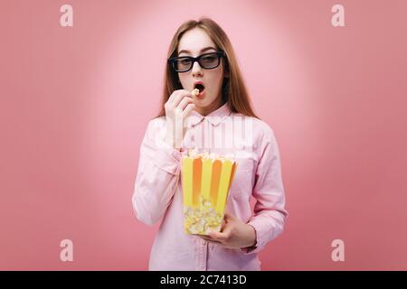 Ritratto di una giovane donna con lunghi capelli biondi guardando la macchina fotografica con espressione emotiva del viso. Ragazza attraente che indossa occhiali 3d e mangiare p Foto Stock