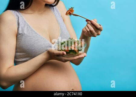 Sorridente donna incinta asiatica mangiare insalata di verdure, primo piano studio isolato shot. Gravidanza, cibo sano e concetto di persone. Foto Stock