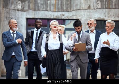 Sei uomini d'affari caucasici e uno africano vestiti in elegante ufficio si muovono energicamente in strada Foto Stock